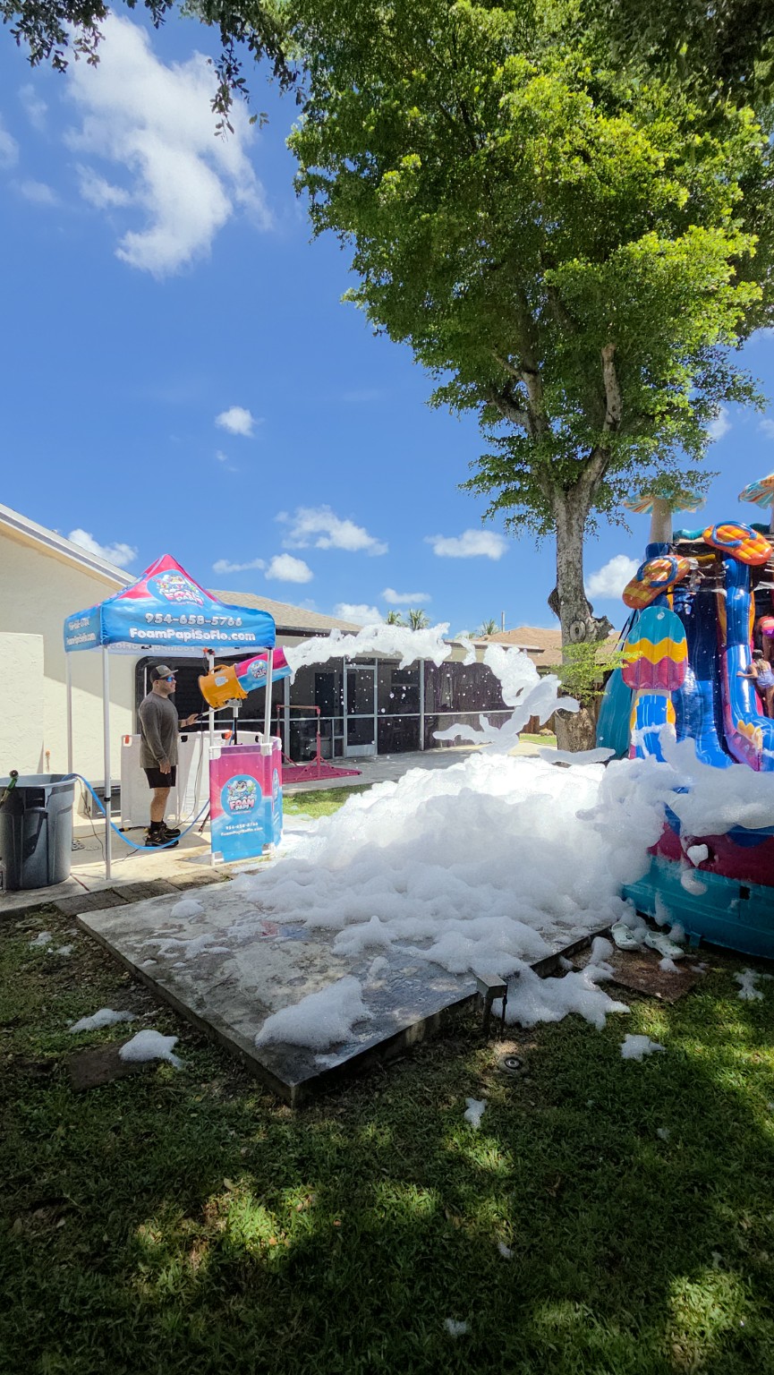 Foam Papi operator filling a backyard party area with foam beside a colorful inflatable